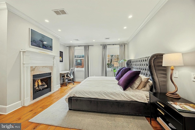 bedroom featuring a fireplace, wood finished floors, visible vents, baseboards, and crown molding