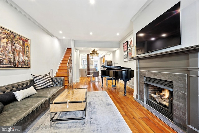 living area with crown molding, hardwood / wood-style floors, a tiled fireplace, baseboards, and stairs