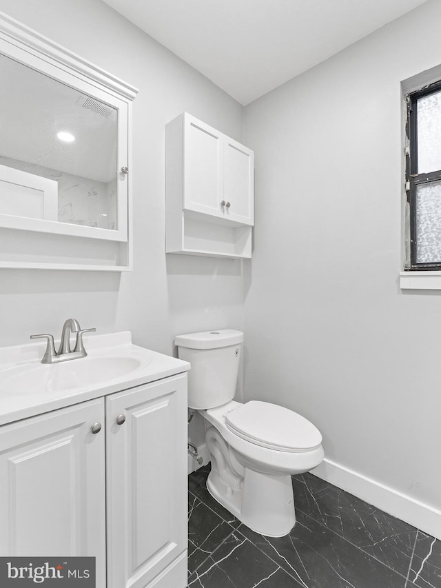 half bath with toilet, marble finish floor, vanity, and baseboards