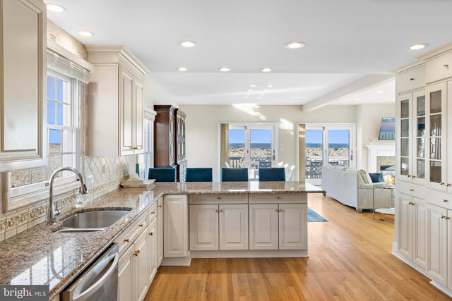 kitchen featuring a peninsula, a fireplace, a sink, dishwasher, and light wood-type flooring