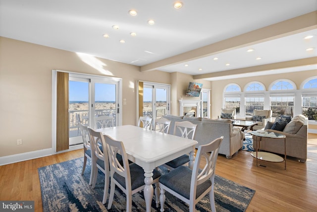 dining room with beam ceiling, recessed lighting, light wood-style floors, a fireplace, and baseboards