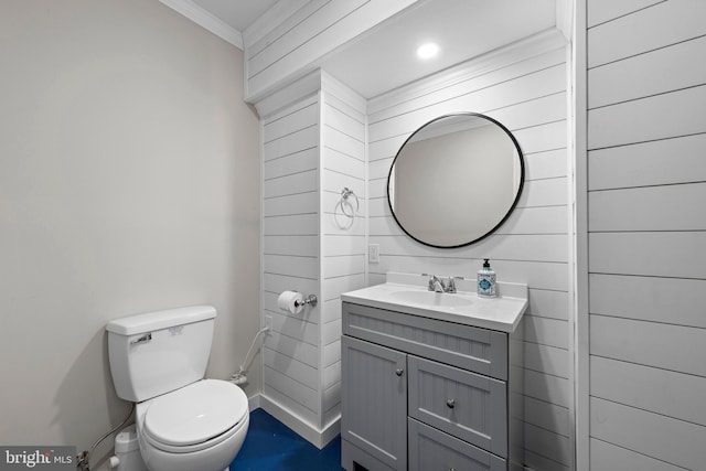 half bathroom with toilet, vanity, baseboards, and ornamental molding