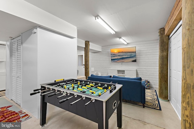 playroom featuring wooden walls and finished concrete flooring