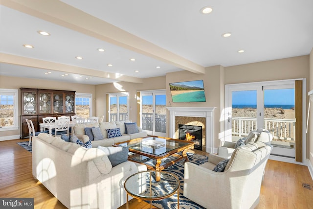 living area featuring beam ceiling, a healthy amount of sunlight, light wood-type flooring, and a high end fireplace