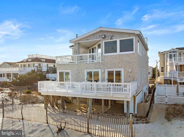 rear view of house featuring a deck, fence, a balcony, and a gate