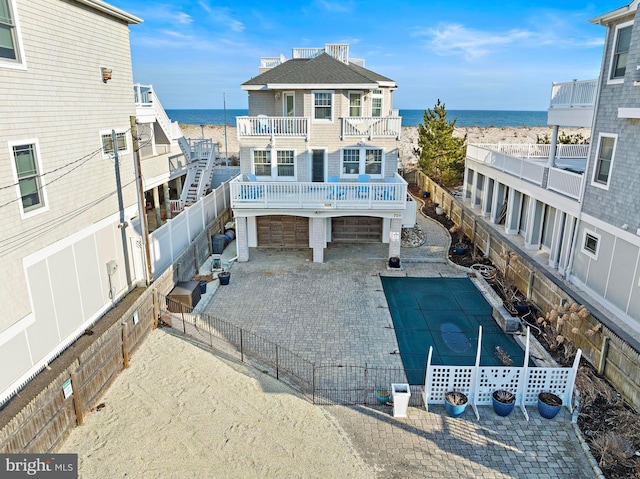 rear view of house featuring a water view, decorative driveway, a fenced backyard, a garage, and a balcony