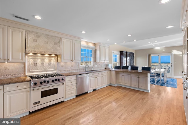 kitchen featuring visible vents, luxury stove, stainless steel dishwasher, custom exhaust hood, and a sink