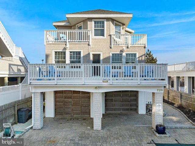 rear view of property featuring decorative driveway, a garage, a balcony, and fence