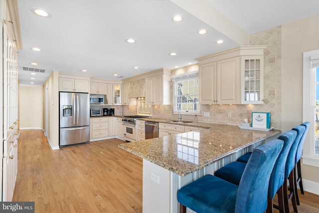 kitchen with a sink, light stone counters, stainless steel appliances, a peninsula, and a breakfast bar area