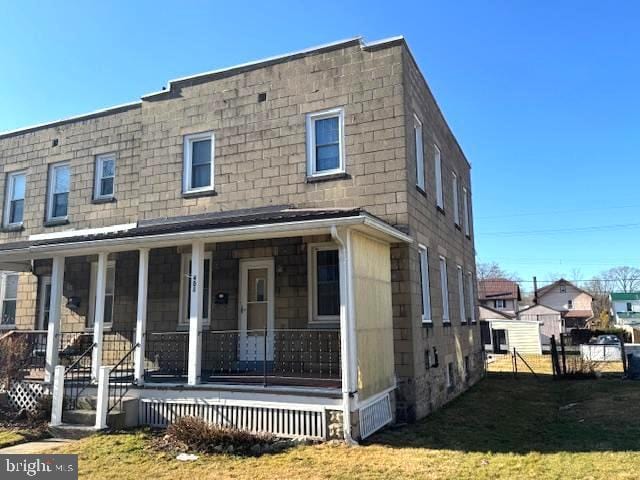 multi unit property featuring covered porch, fence, and a front lawn