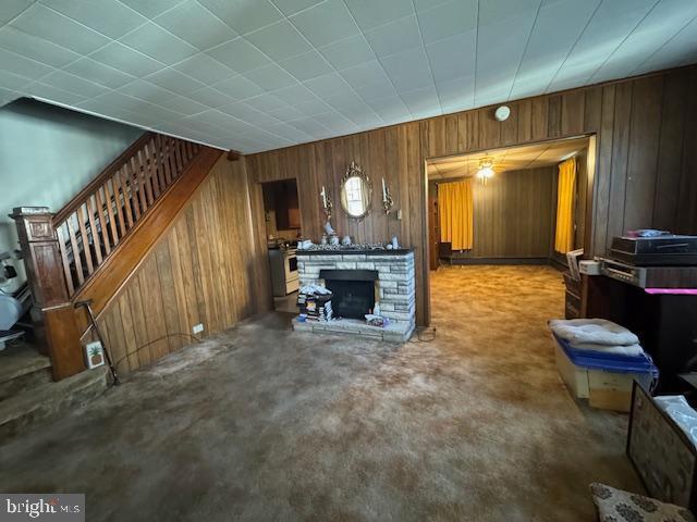 living area with wood walls, stairway, and a stone fireplace