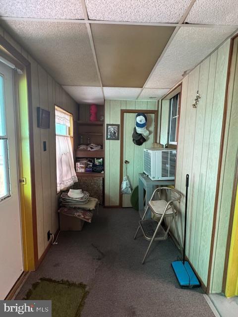 interior space with cooling unit, carpet flooring, wood walls, and a drop ceiling