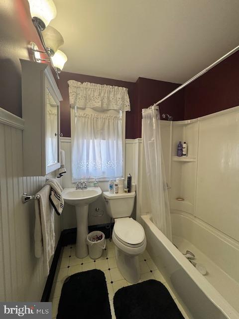 bathroom with toilet, a wainscoted wall, a sink, and shower / bath combination with curtain