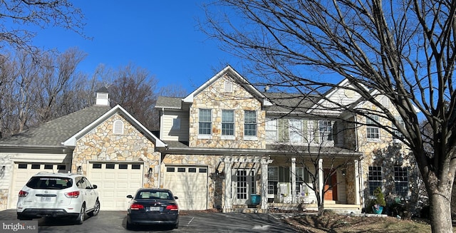 view of front of house featuring aphalt driveway, stone siding, roof with shingles, a garage, and a chimney