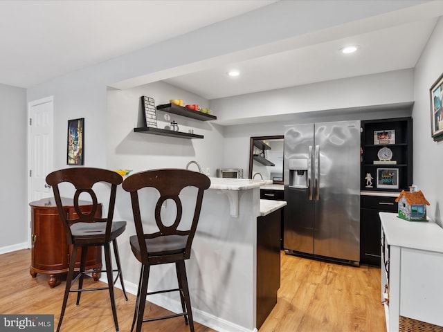 kitchen featuring open shelves, light wood-style flooring, a kitchen bar, and stainless steel refrigerator with ice dispenser