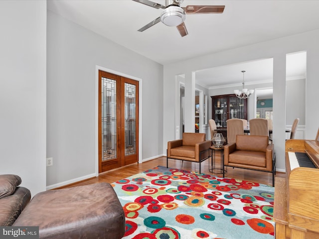 living area featuring baseboards, ornamental molding, wood finished floors, and ceiling fan with notable chandelier