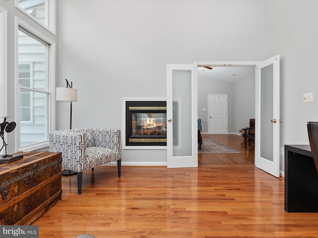 sitting room with baseboards, a multi sided fireplace, a towering ceiling, and light wood-type flooring