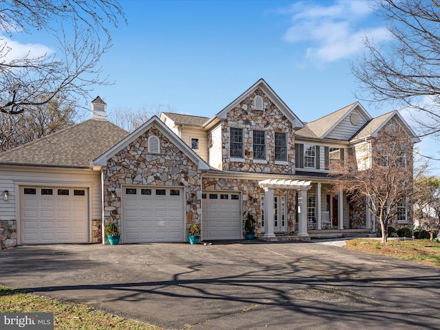 view of front of house featuring stone siding, a chimney, driveway, and an attached garage