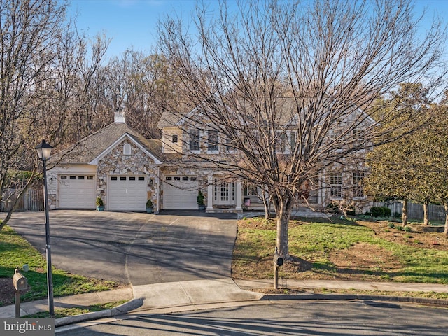 view of front facade with stone siding, aphalt driveway, fence, a chimney, and an attached garage