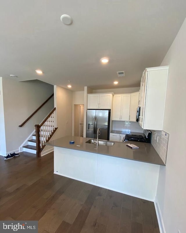 kitchen with a peninsula, a sink, white cabinets, stainless steel refrigerator with ice dispenser, and dark wood finished floors