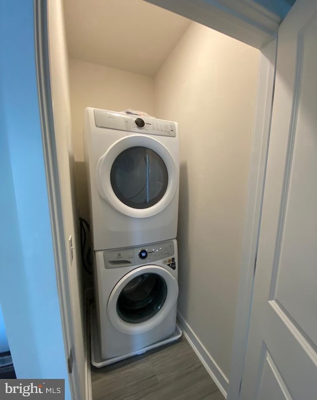 washroom featuring baseboards, laundry area, wood finished floors, and stacked washer / drying machine