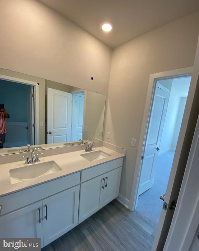 bathroom featuring wood finished floors, a sink, baseboards, and double vanity