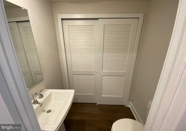 bathroom featuring toilet, wood finished floors, a sink, baseboards, and a closet