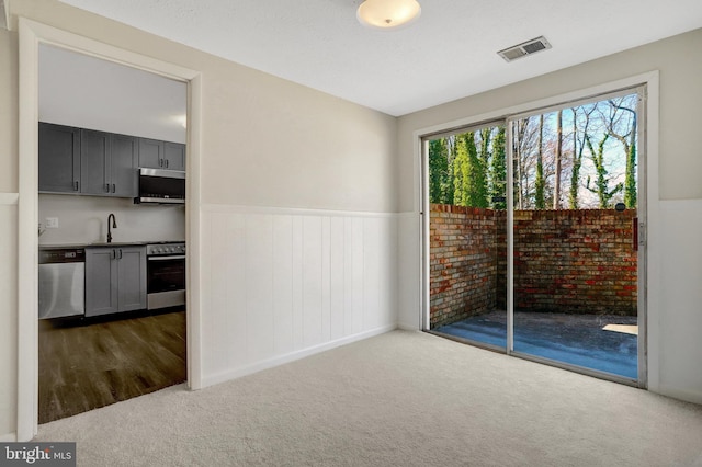 unfurnished room with visible vents, wainscoting, a sink, and carpet floors