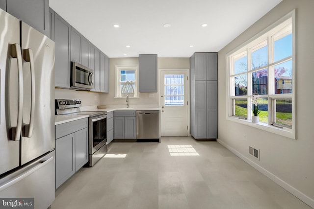 kitchen featuring visible vents, gray cabinets, a sink, appliances with stainless steel finishes, and baseboards