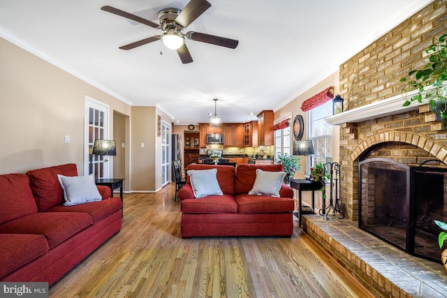 living area featuring ornamental molding, wood finished floors, baseboards, a brick fireplace, and ceiling fan