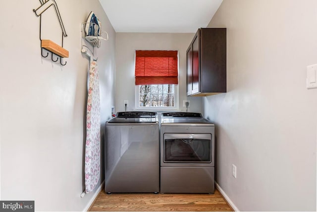 clothes washing area with cabinet space, light wood-style flooring, baseboards, and separate washer and dryer