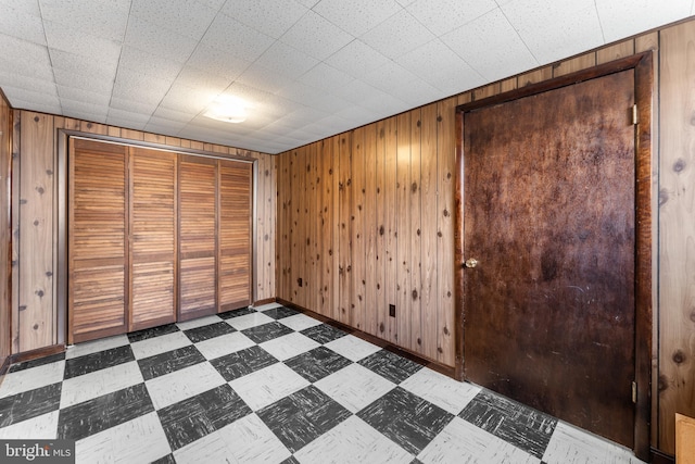 unfurnished bedroom featuring tile patterned floors, wooden walls, baseboards, and a closet