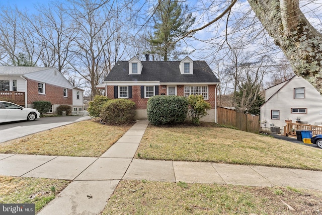 cape cod home with brick siding, a shingled roof, a front yard, and fence