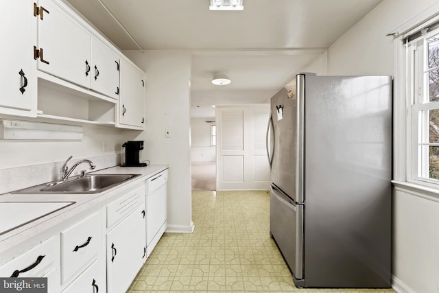 kitchen with light floors, dishwasher, freestanding refrigerator, white cabinets, and a sink