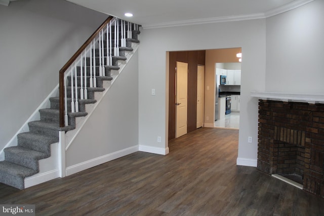 interior space featuring stairway, crown molding, baseboards, a brick fireplace, and dark wood-style floors
