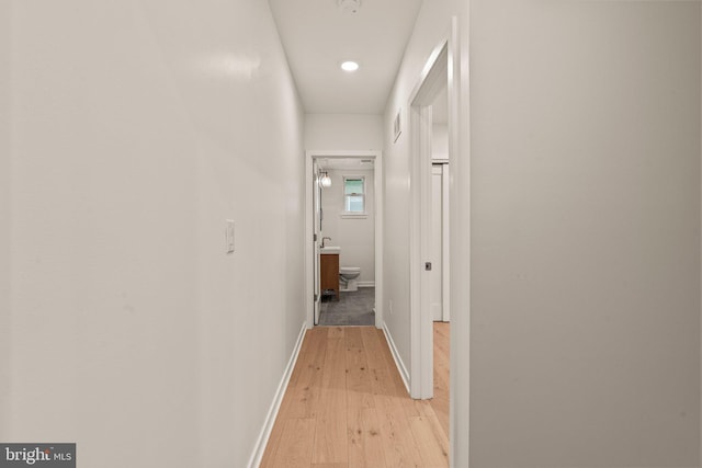 corridor featuring baseboards, visible vents, and light wood finished floors