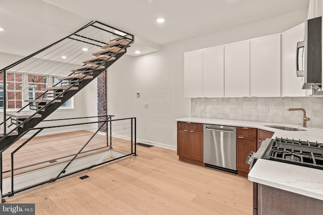 kitchen with appliances with stainless steel finishes, backsplash, white cabinetry, and light wood-style flooring