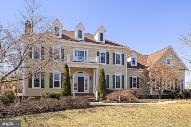 colonial inspired home with a balcony and a front lawn