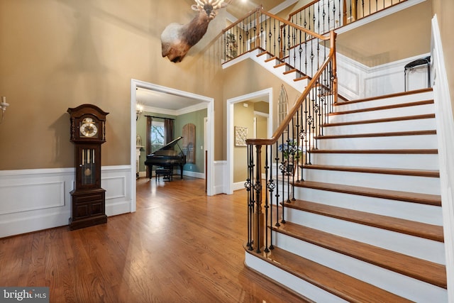 foyer entrance with stairway, wainscoting, a high ceiling, and wood finished floors