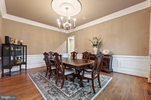 dining room with an inviting chandelier, wood finished floors, wainscoting, and crown molding