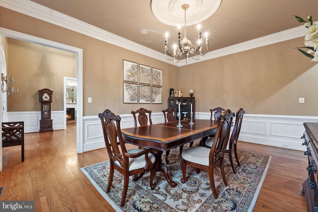 dining room with crown molding, a notable chandelier, wood finished floors, and a lit fireplace