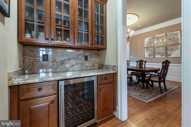 bar with light wood-type flooring, wine cooler, a bar, crown molding, and decorative backsplash