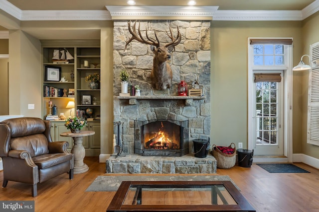 sitting room featuring baseboards, wood finished floors, a stone fireplace, and ornamental molding