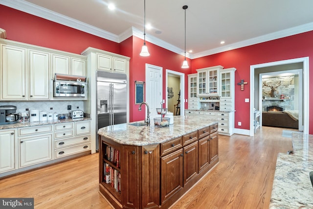 kitchen featuring a warm lit fireplace, ornamental molding, a sink, built in appliances, and white cabinetry