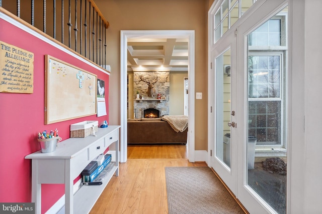 doorway to outside featuring wood finished floors, baseboards, coffered ceiling, beam ceiling, and a stone fireplace