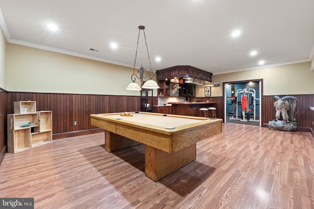 rec room featuring light wood finished floors, crown molding, a wainscoted wall, indoor wet bar, and recessed lighting