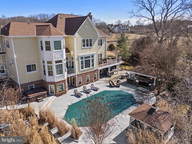 back of property with brick siding, a covered pool, a hot tub, a chimney, and a patio area