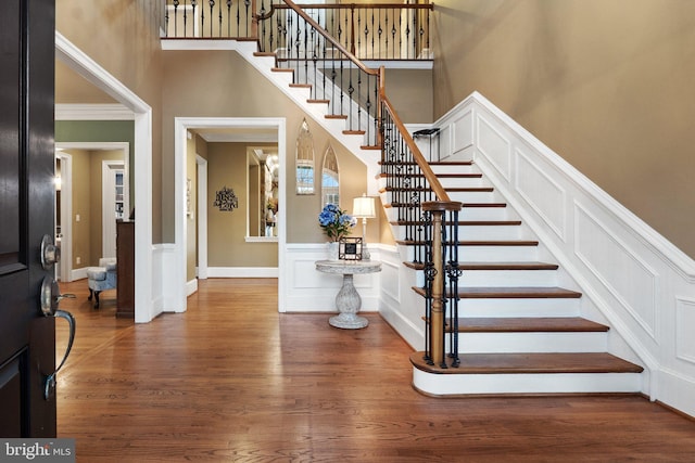 stairway featuring a decorative wall, crown molding, a towering ceiling, and wood finished floors