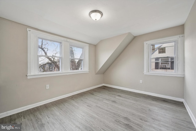 additional living space with baseboards, vaulted ceiling, a wealth of natural light, and wood finished floors