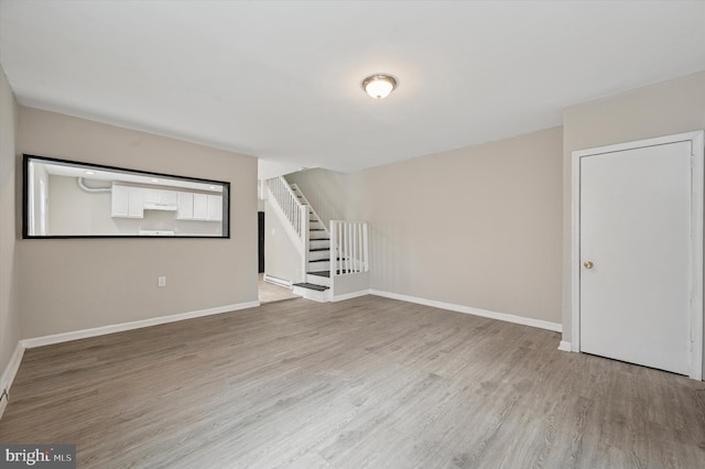 empty room featuring light wood-style floors, stairs, and baseboards